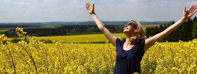 woman in a field of yellow flowers with arms raised in worship to God