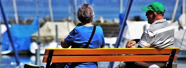 Senior adults sitting on a park bench looking at the ocean