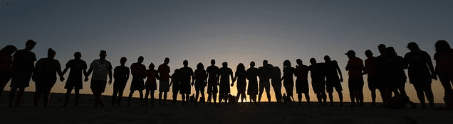A large group of different people in a line together at sunset