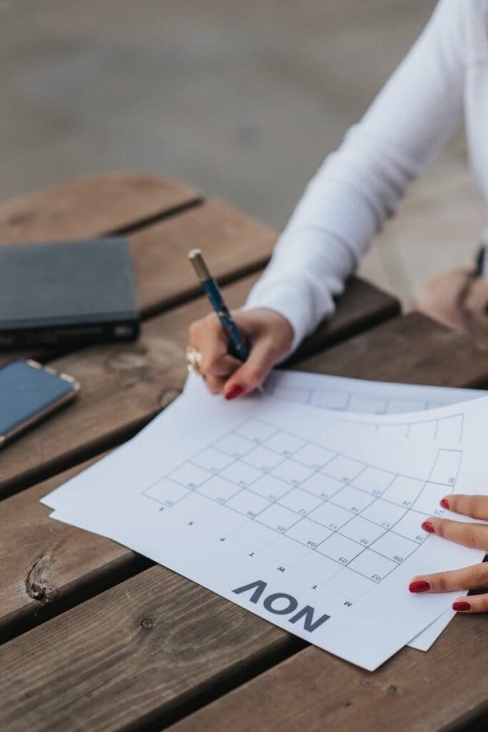 A woman writes on a November calendar outdoors, planning and scheduling her month.
